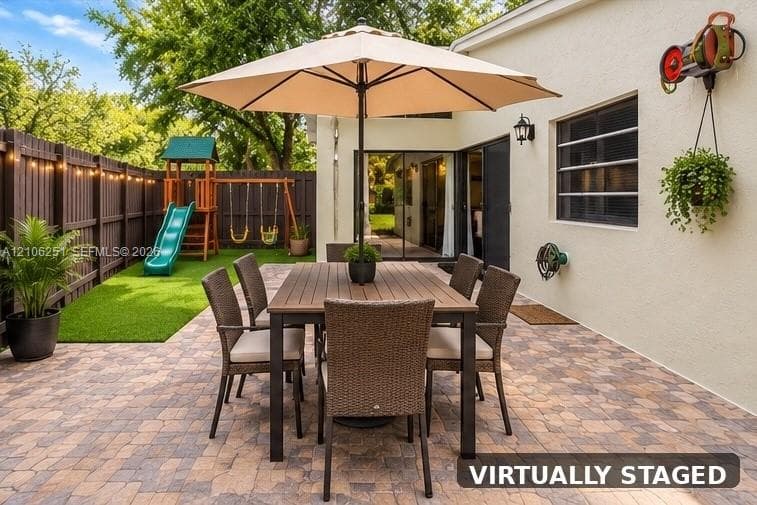 Paver patio featuring string lighting, artificial turf, perimeter wood privacy fencing, and sliding glass door access