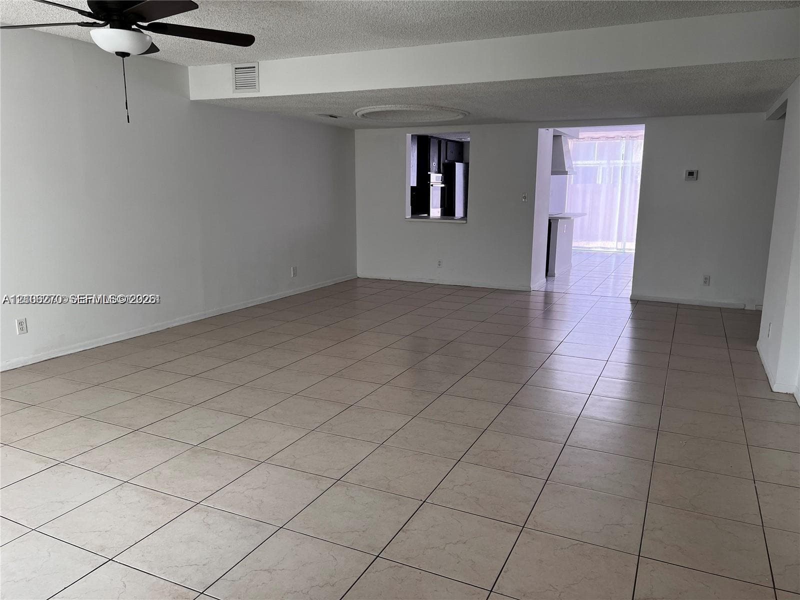 Open floor plan featuring neutral ceramic tile flooring, ceiling fan with integrated lighting, and a pass-through window