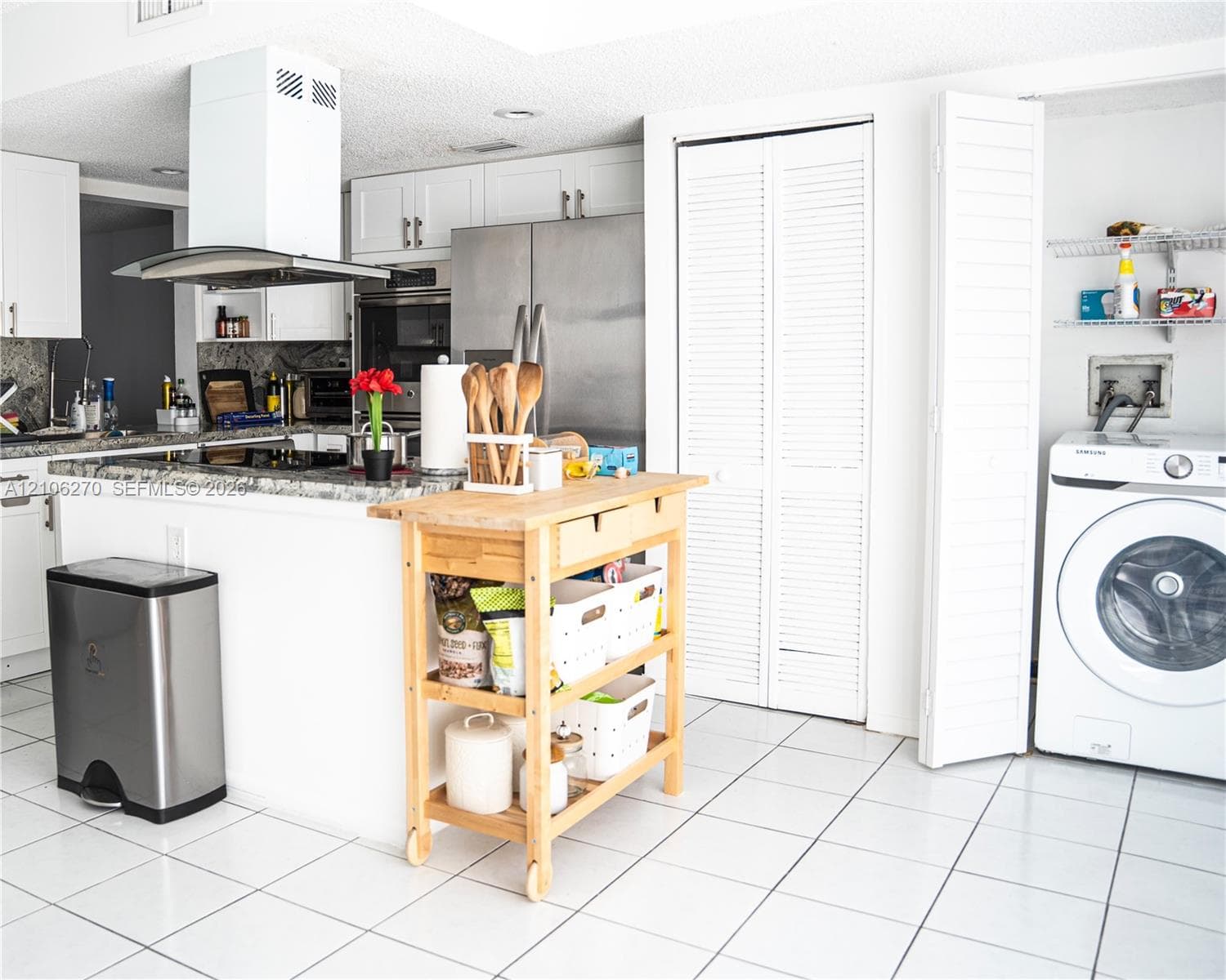 Kitchen featuring white cabinetry, stone countertops, stainless steel appliances, a chimney-style range hood, and tile flooring