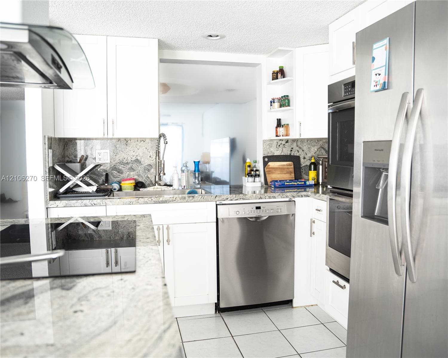 Kitchen featuring white cabinetry, stone countertops, integrated stainless steel appliances, open shelving, and tile flooring