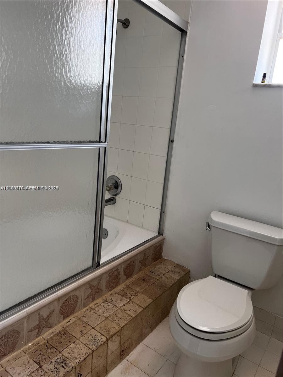 Bathtub and shower combination featuring a metal-framed glass enclosure, white wall tiling, and a decorative tile surround with a coastal motif