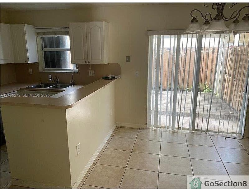 Kitchen featuring white cabinetry, a dual-basin sink, a raised breakfast bar, ceramic tile flooring, and a sliding glass door
