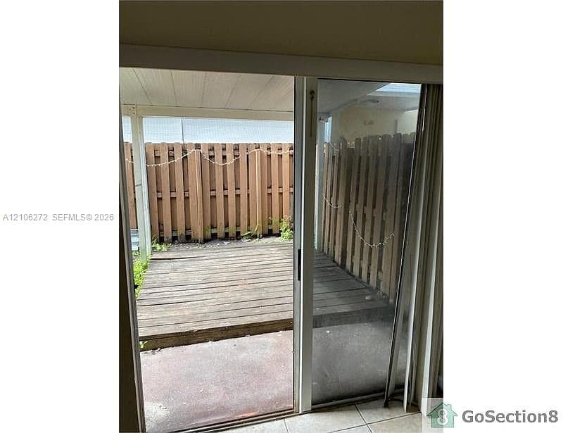 Sliding glass door opening to a private outdoor space featuring a wood-plank deck, covered patio area, and wood privacy fencing