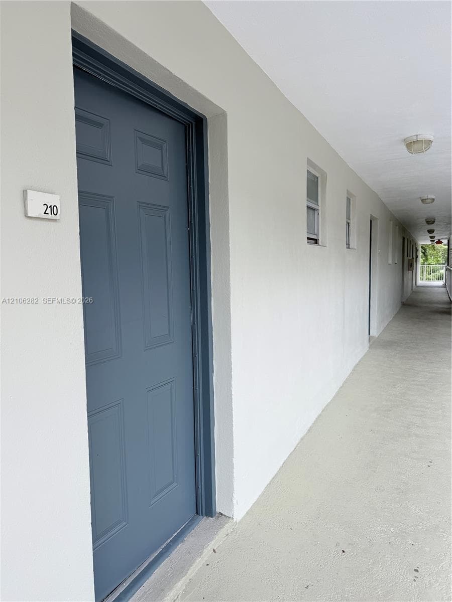 Exterior entrance featuring a paneled door, flush-mounted wall lighting, and concrete-finish walkway