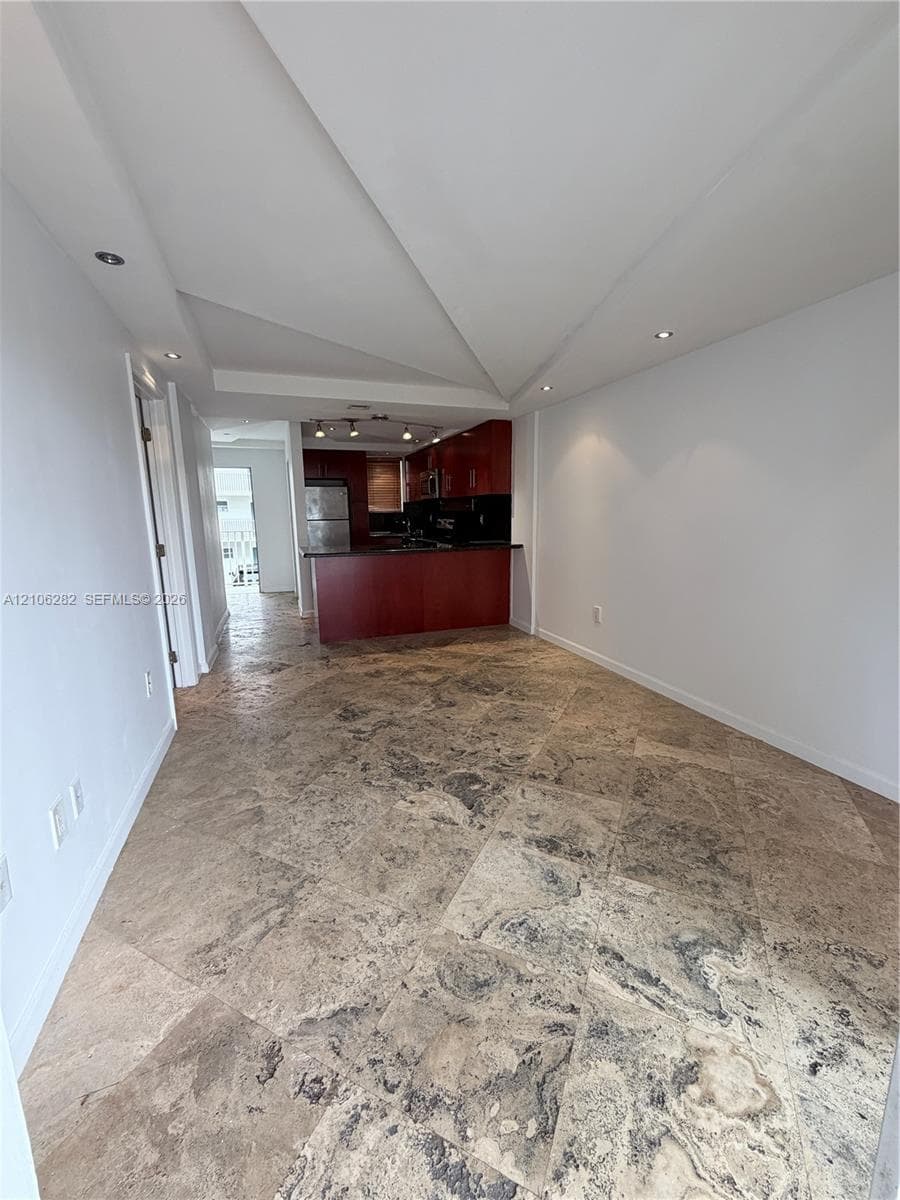 Open-concept area featuring stone tile flooring, custom architectural ceiling design, recessed lighting, and a dark wood-finish kitchen cabinetry island
