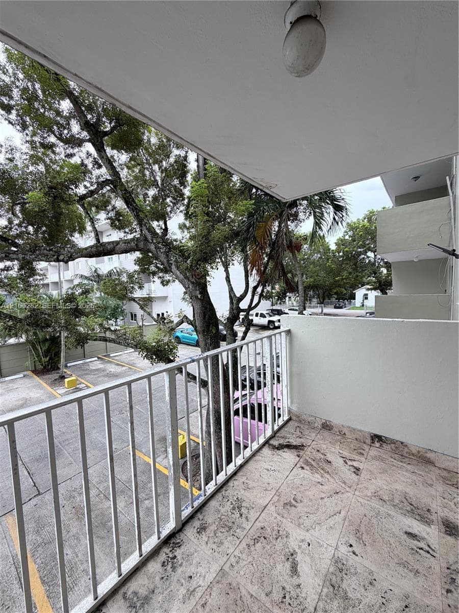 Covered balcony featuring stone-finish flooring, a white metal railing, and an integrated ceiling light fixture