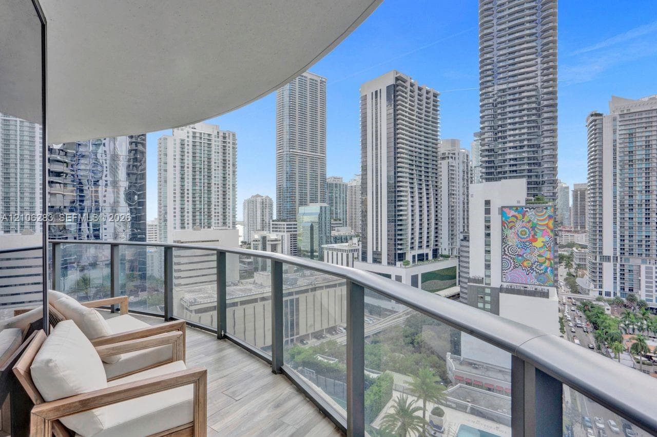 Private balcony with tile flooring and a glass-paneled railing overlooking an urban cityscape