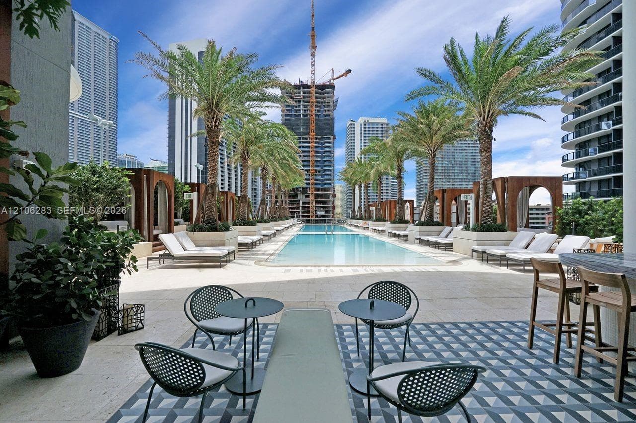Pool deck featuring a linear swimming pool, geometric tile flooring, wood-framed cabanas, and perimeter palm trees