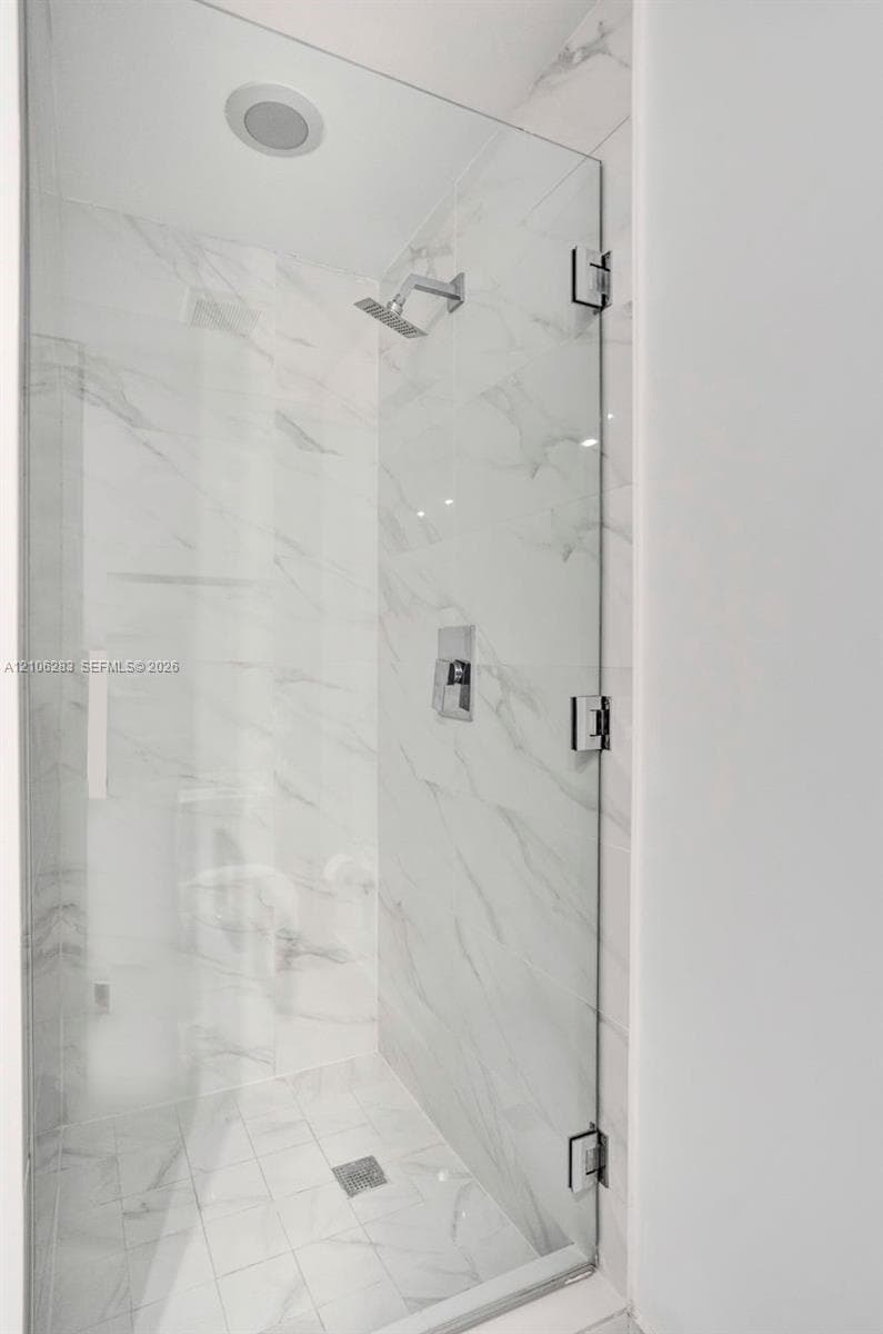 Walk-in shower featuring a frameless glass door, wall-to-wall stone-finish tile, recessed ceiling light, and polished chrome fixtures