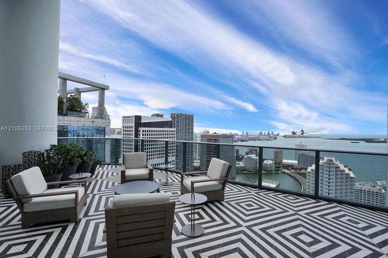 Expansive covered terrace featuring black and white geometric tile flooring, a glass-panel railing, and panoramic water and city skyline outlooks