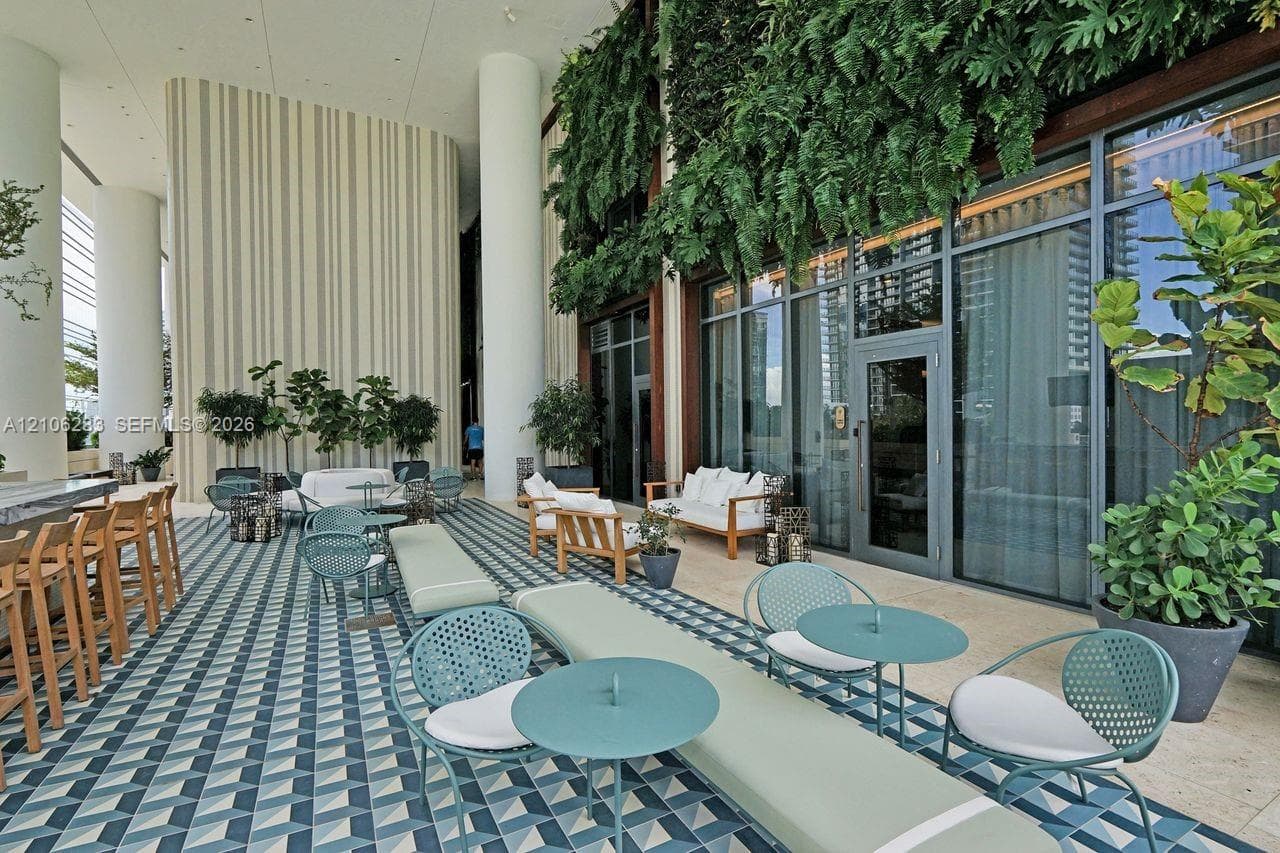 Covered outdoor terrace featuring geometric patterned tile flooring, floor-to-ceiling glass paneling, vertical green wall accents, and structural columns