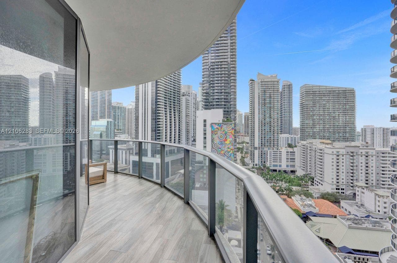 Curved balcony featuring wood-finish flooring, floor-to-ceiling glass railings, and expansive urban skyline scenery
