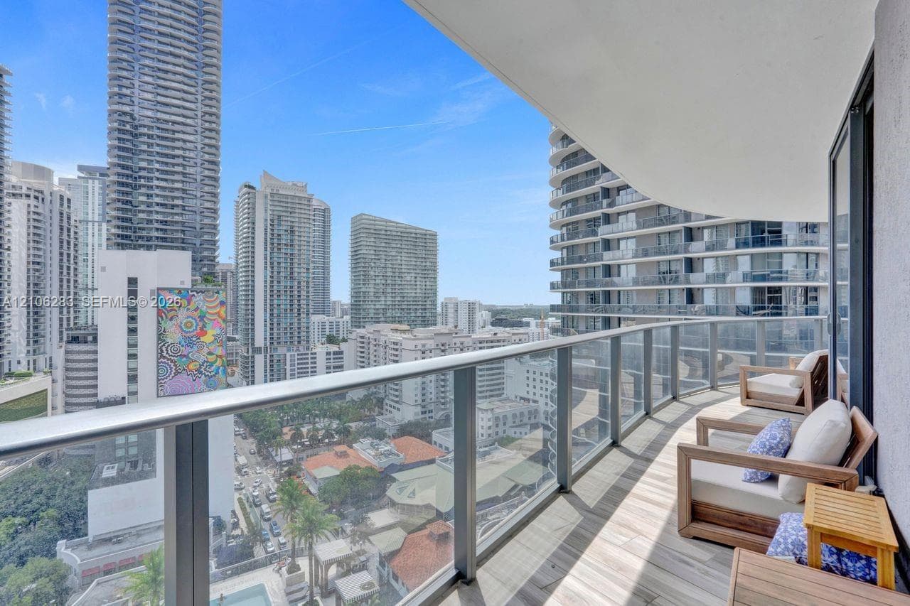 Covered balcony featuring wood-finish flooring, glass-panel railing, and a metal handrail