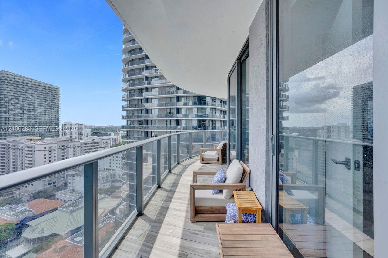 Covered balcony featuring wood-finish flooring, glass panel railings, and full-height sliding glass doors