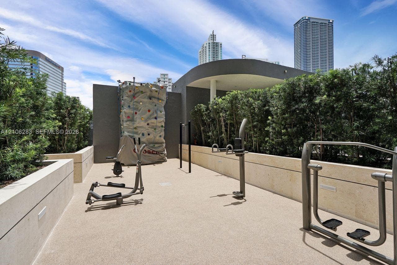 Outdoor fitness space featuring a climbing wall, anchored exercise equipment, stone-finish retaining walls, and a manicured hedge perimeter