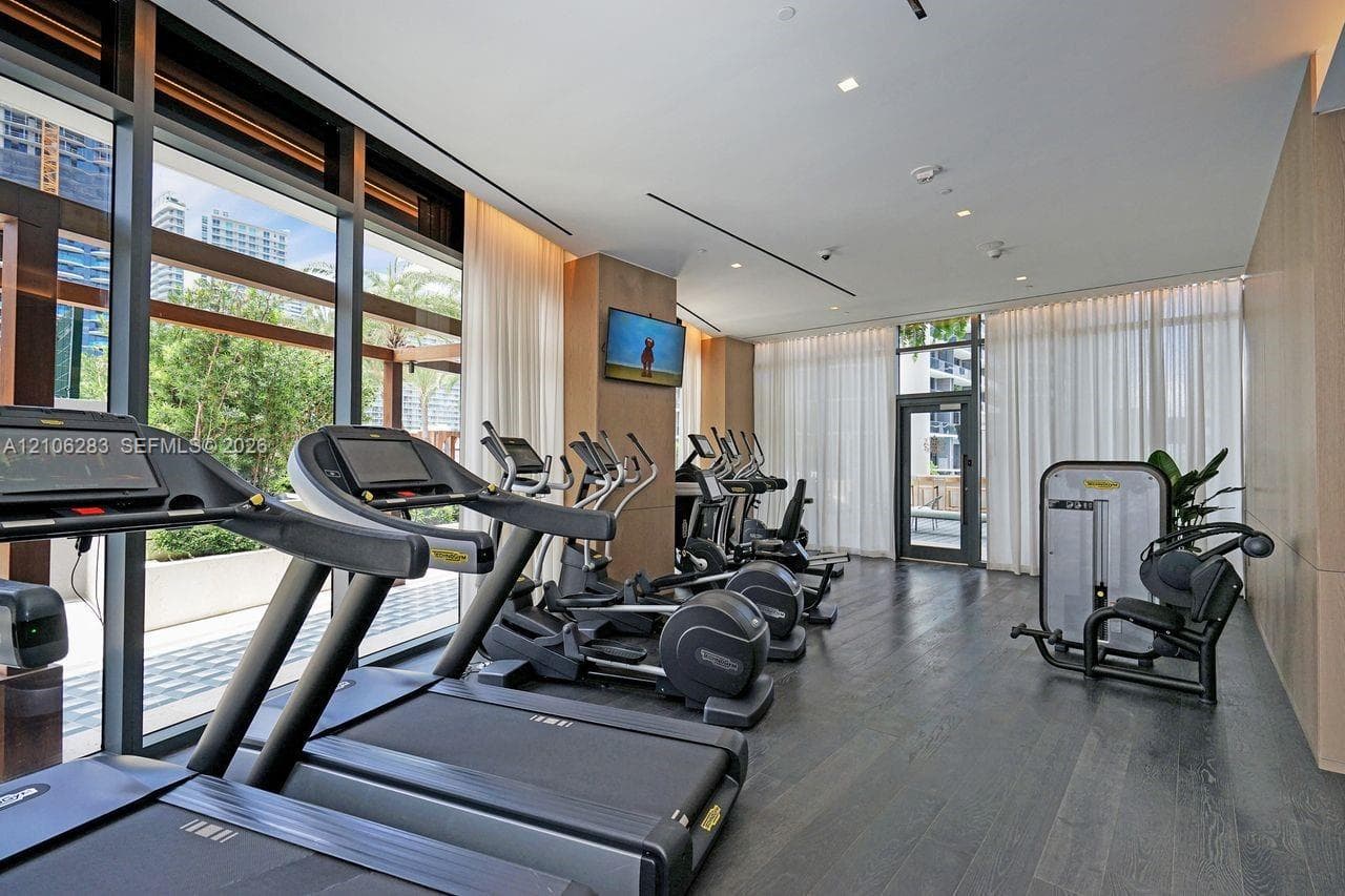 Fitness center featuring dark wood-finish flooring, floor-to-ceiling windows, recessed lighting, and wall-mounted neutral paneling