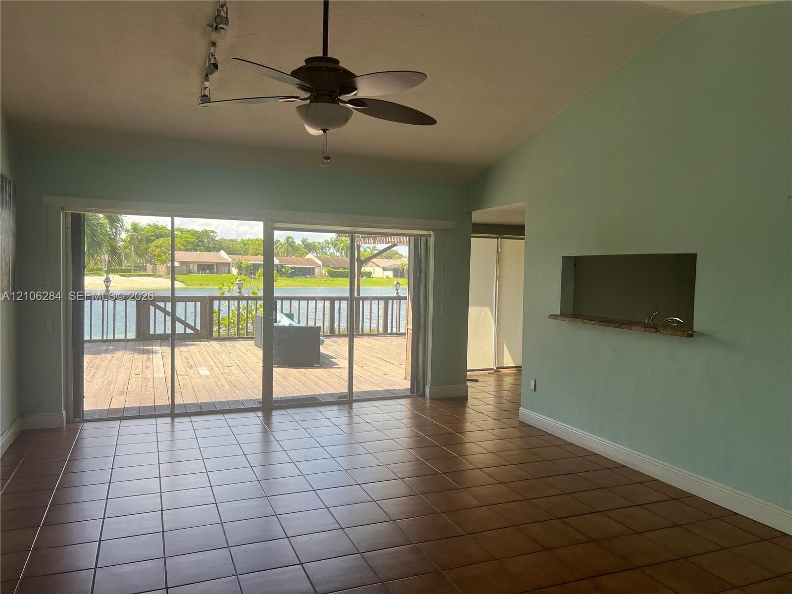 Ceramic tile flooring, vaulted ceilings, ceiling fan, pass-through window with shelf, and large sliding glass doors opening to a wood deck