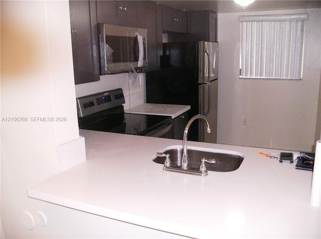 Kitchen featuring dark cabinetry, stainless steel appliances, solid-surface countertops, and a dual-handle gooseneck faucet