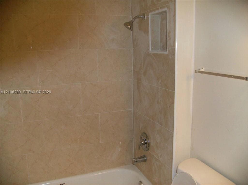 Bathtub enclosure featuring large-format ceramic tile surround, integrated shower niche, chrome plumbing fixtures, and wall-mounted metal towel bar