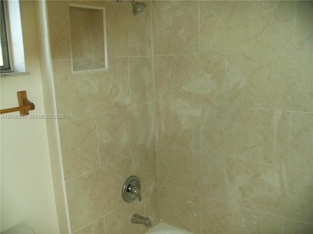 Full-height ceramic wall tiling featuring a neutral veined pattern, integrated recessed shelving, and a brushed metallic shower and tub faucet set