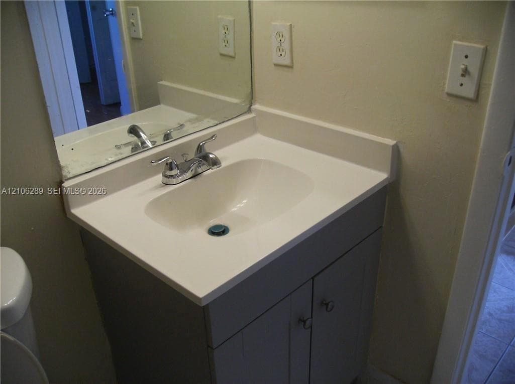 Vanity featuring a solid surface countertop with an integrated basin, chrome-finish dual-handle faucet, gray cabinetry, and a wall-mounted mirror