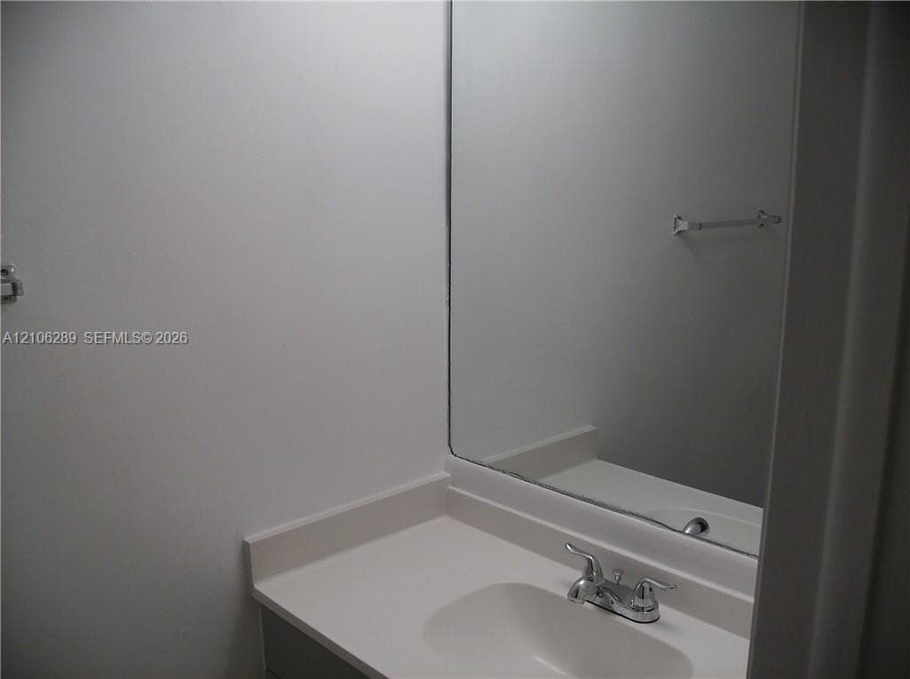 Vanity with integrated sink, solid surface countertop, chrome dual-handle faucet, and rectangular wall-mounted mirror with attached towel bar