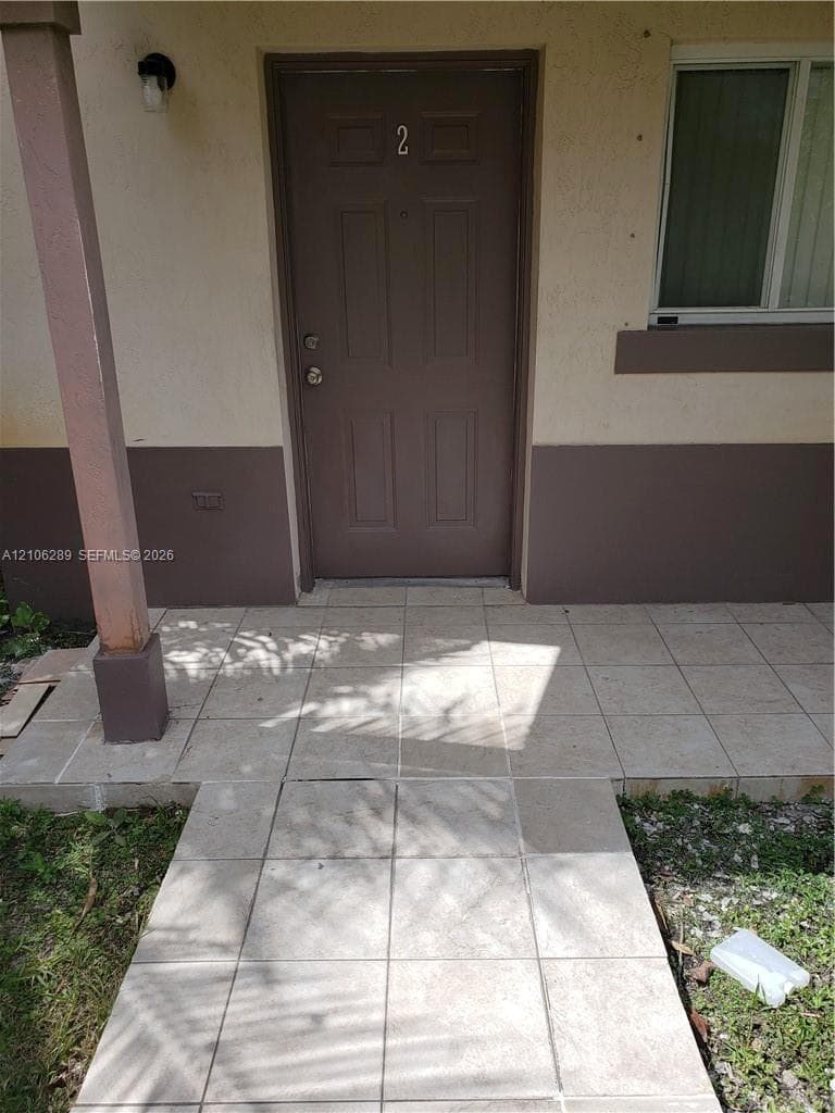 Entrance featuring a four-panel door, tiled patio, and exterior wall-mounted lighting fixture