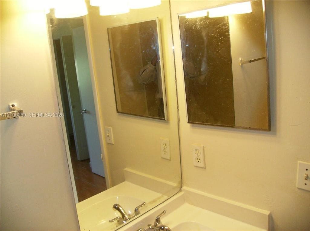 Integrated vanity with a white countertop and recessed basin, wall-mounted mirror, metal faucet hardware, and multi-bulb overhead light fixture