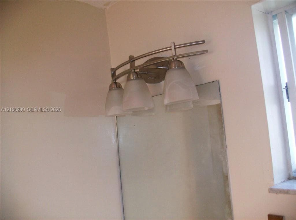 Brushed nickel three-light vanity fixture with frosted glass shades, mounted above a rectangular wall mirror and single-pane window