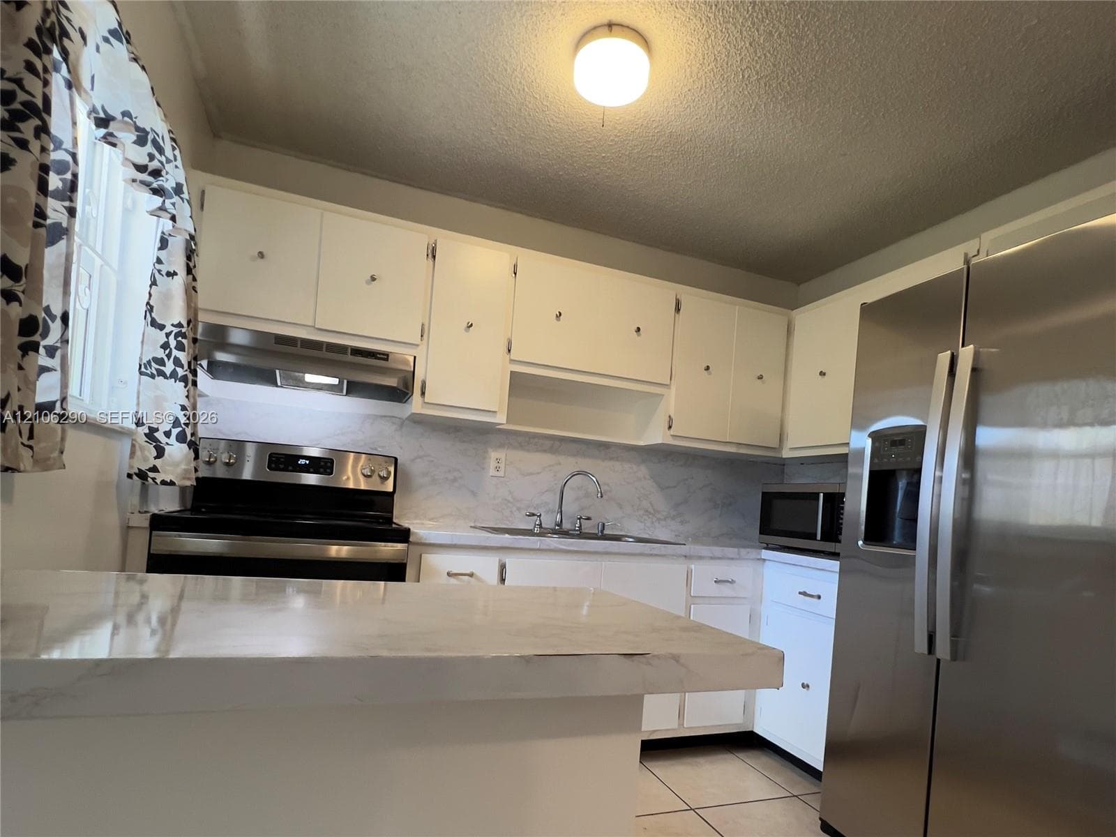 Kitchen featuring white cabinetry, stainless steel refrigerator, integrated range, and tile flooring