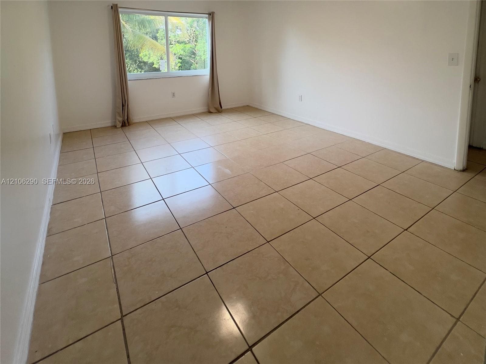 Spacious room featuring neutral ceramic tile flooring, smooth white walls, and large sliding impact window