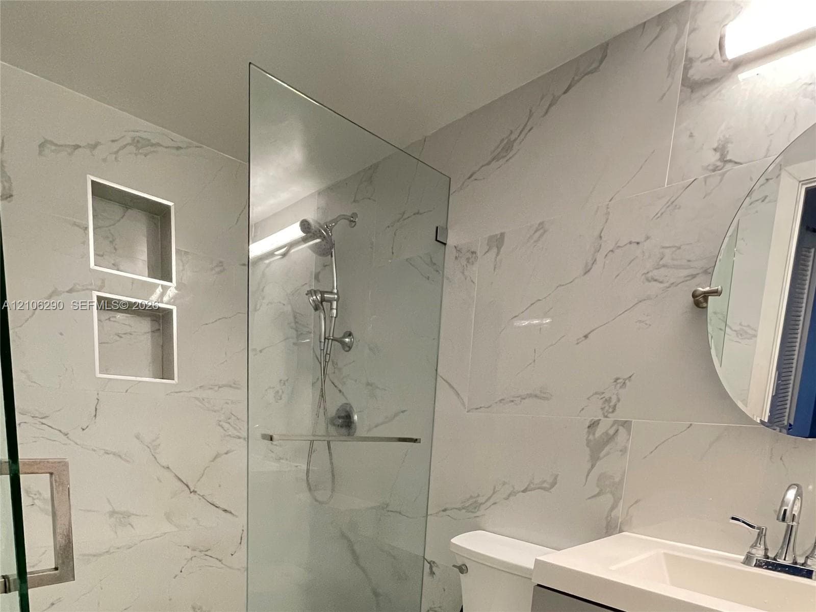 Walk-in shower featuring a frameless glass enclosure, dual built-in wall niches, large-format veined tile surround, and polished chrome fixtures