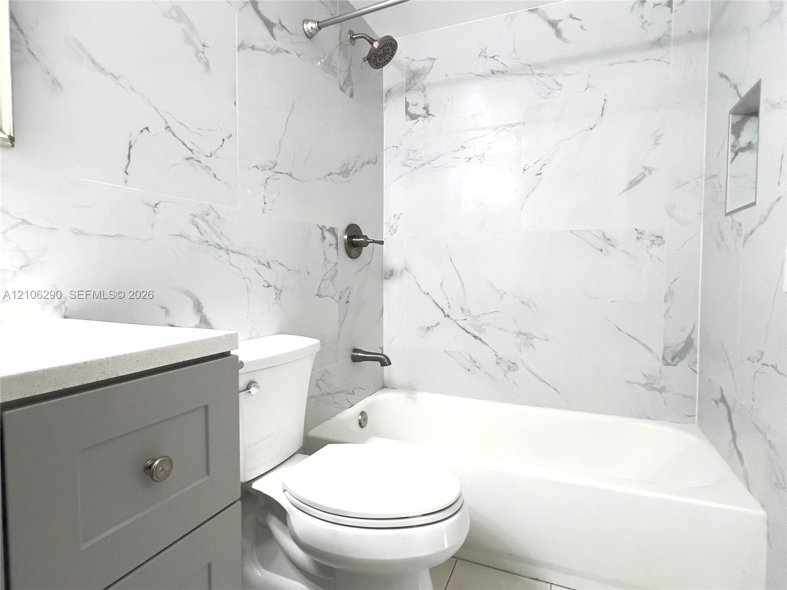Grey vanity featuring a countertop with an integrated basin, three drawers, and two cabinets, complemented by large-format porcelain tile flooring and wall surfacing with a veined pattern