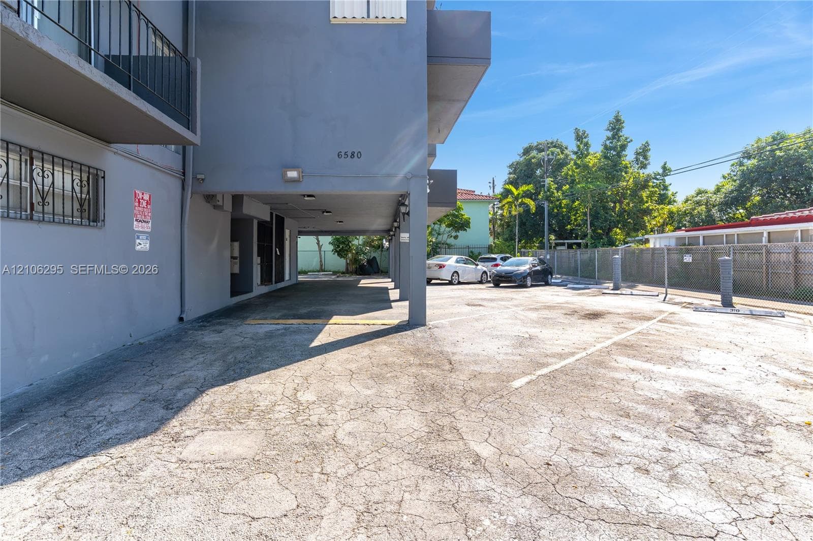 Covered ground-level parking area with paved surface and metal perimeter fencing