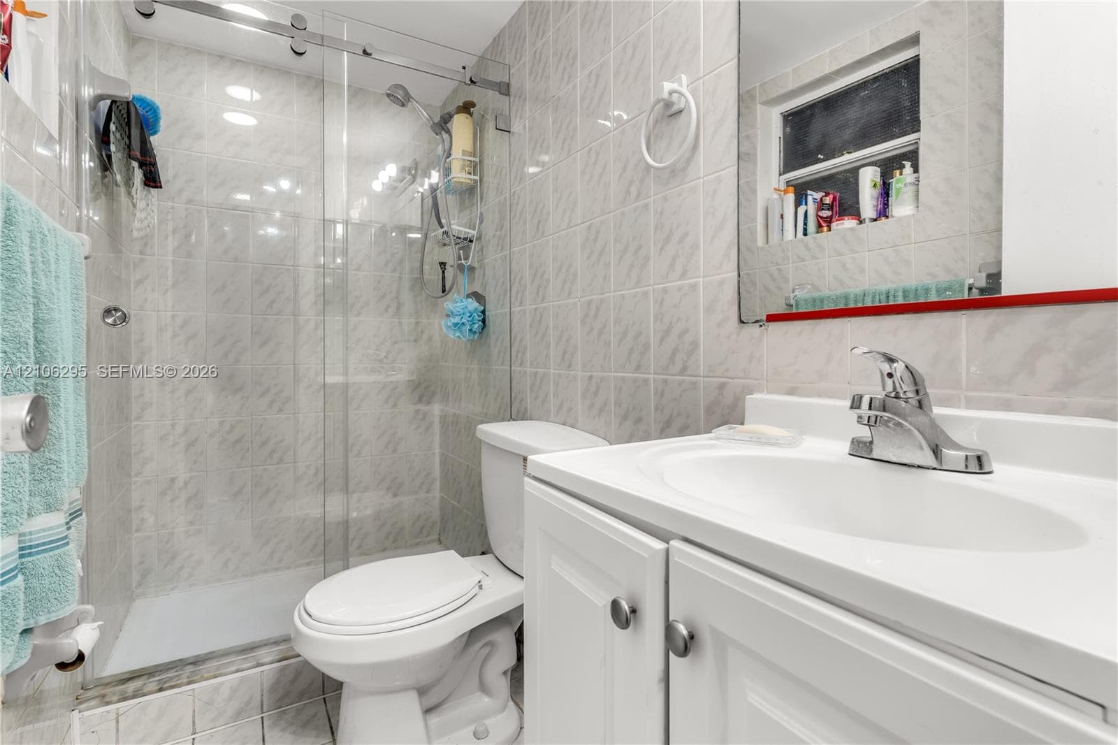 Bathroom featuring a walk-in shower with sliding glass doors, floor-to-ceiling tile work, and a white vanity with an integrated sink