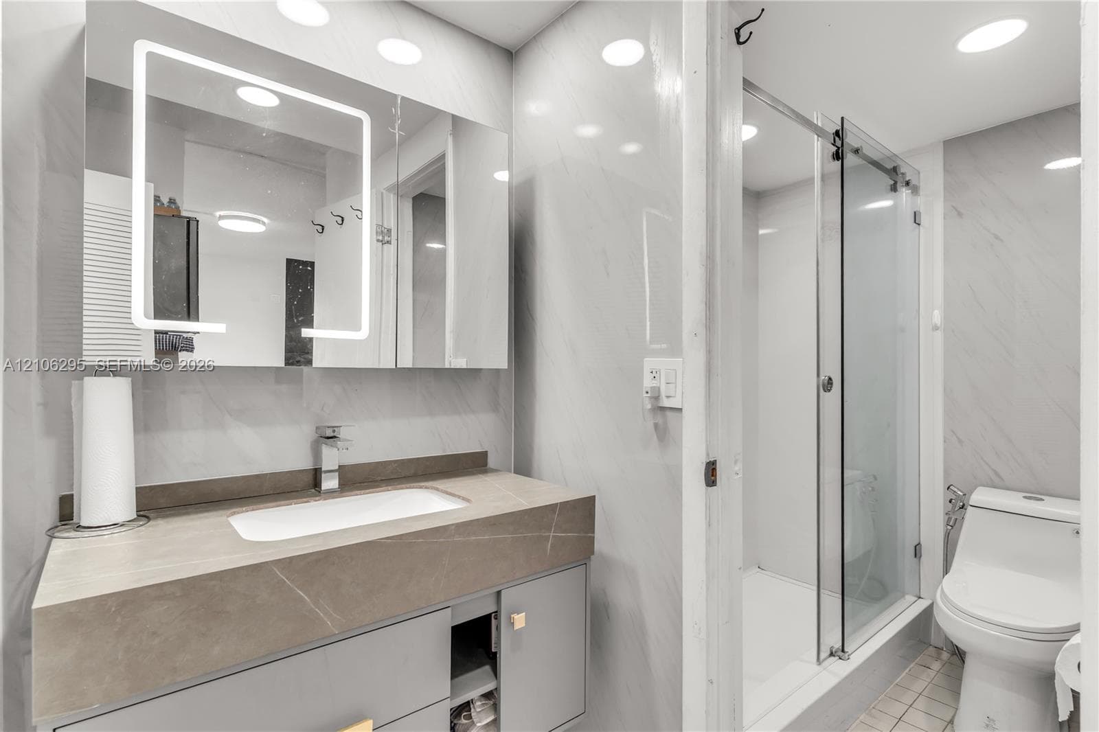 Bathroom featuring a vanity with a stone-finish countertop, undermount sink, and integrated LED-lit medicine cabinet, paired with a glass-enclosed shower and tiled wall surfaces