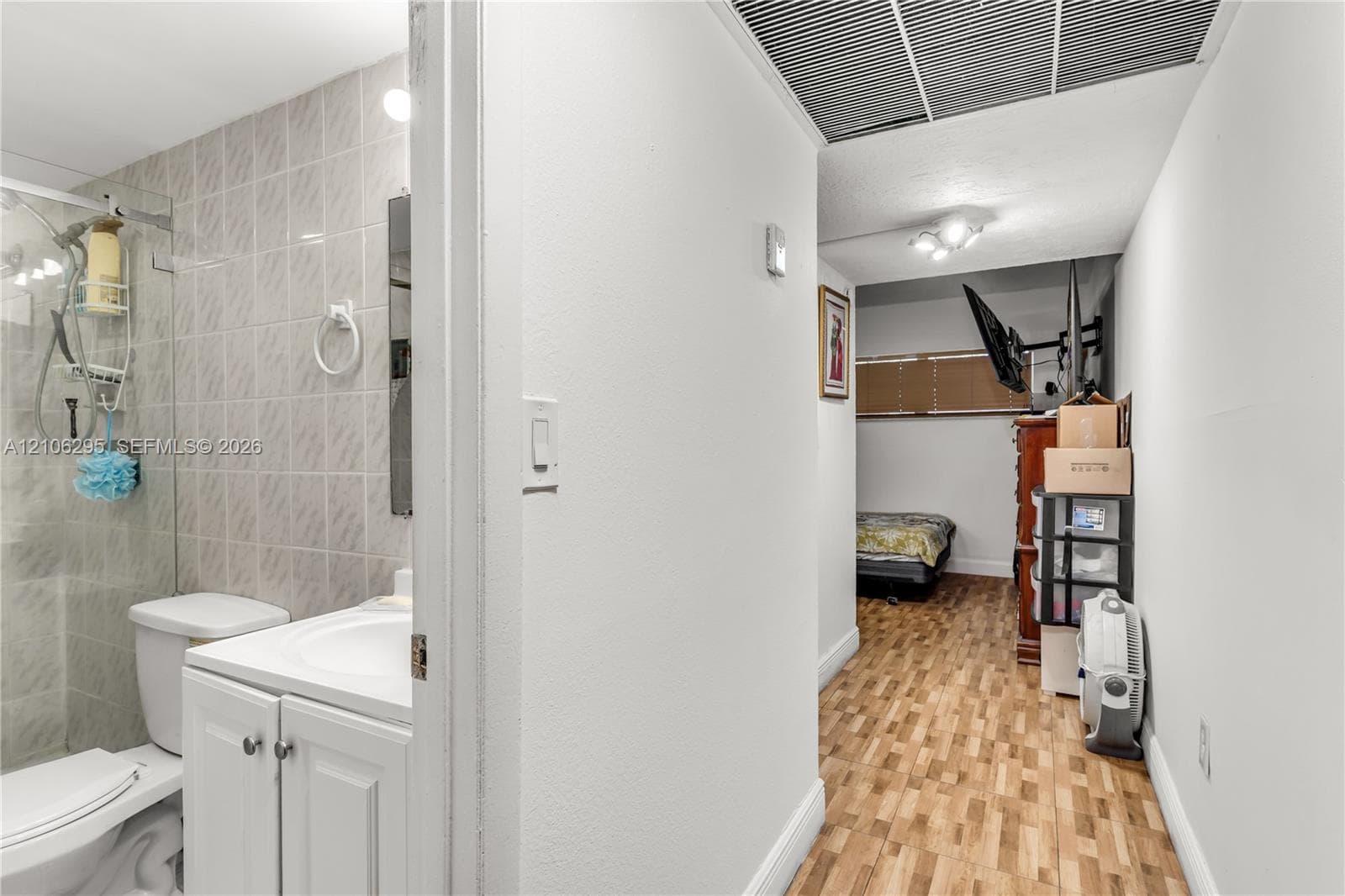 Bathroom featuring a white vanity cabinet with a integrated sink, a glass-enclosed shower with tiled walls, and wood-finish flooring throughout