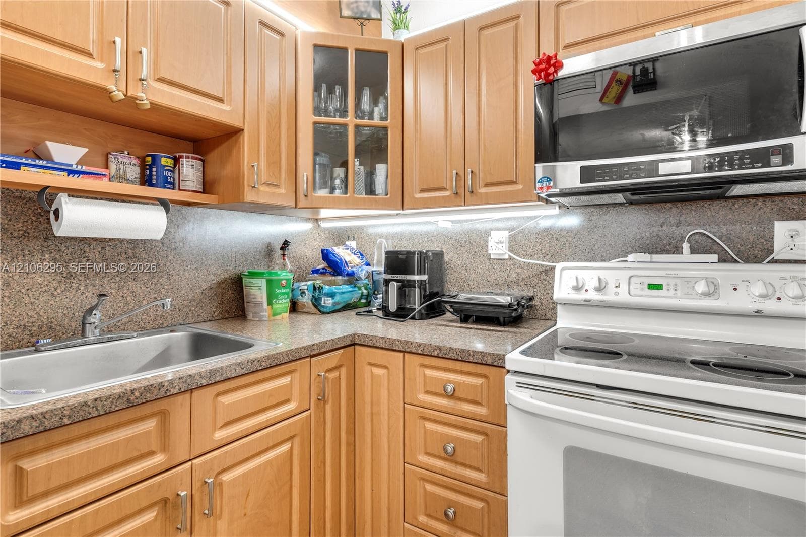 Kitchen featuring natural-finish wood cabinetry, integrated glass-front display doors, stone-composite countertops, stainless steel sink with pull-out faucet, and built-in microwave