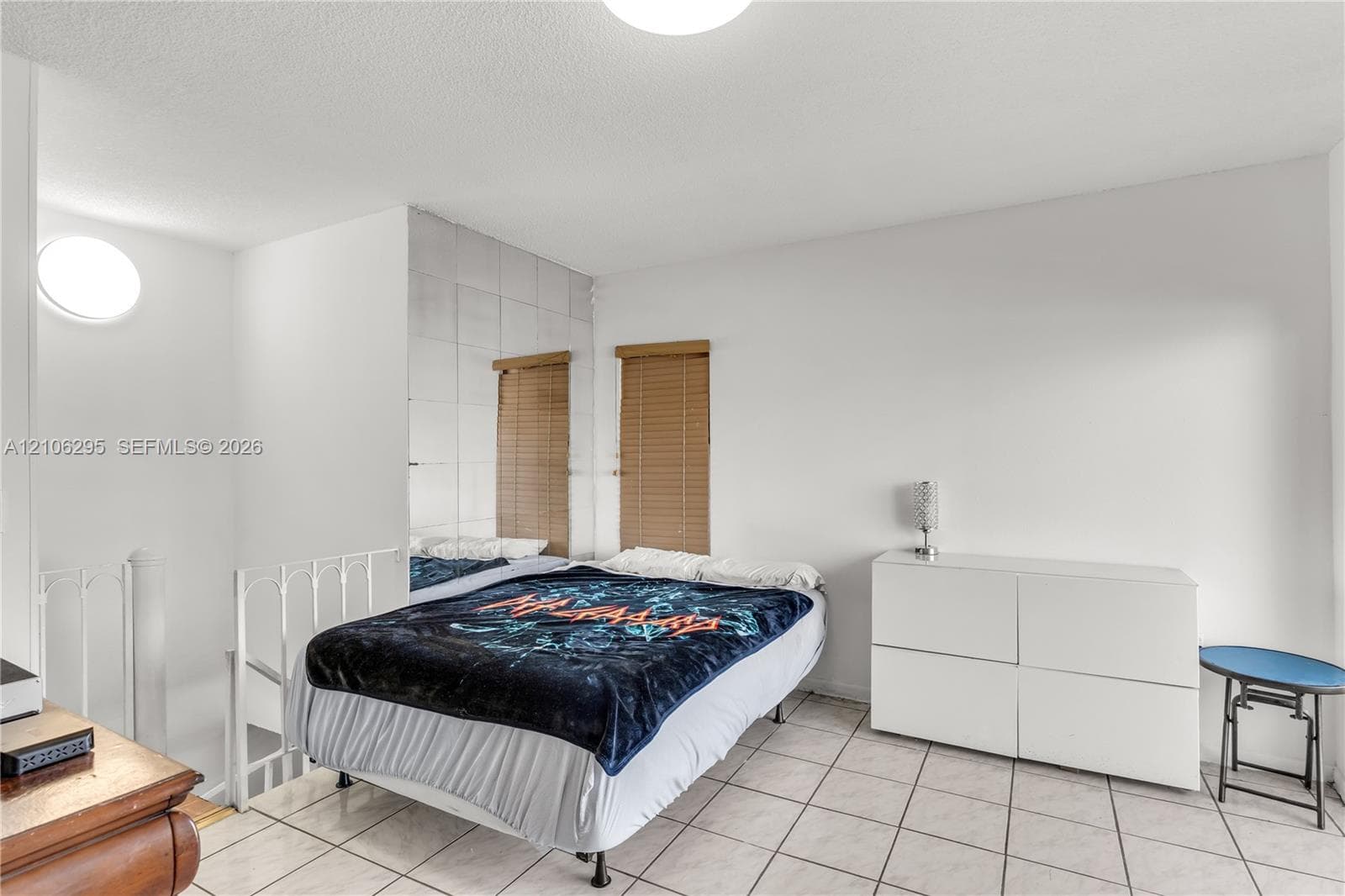 Ceramic tile flooring, white wall-mounted light fixtures, mirrored wall paneling, and a metal staircase railing