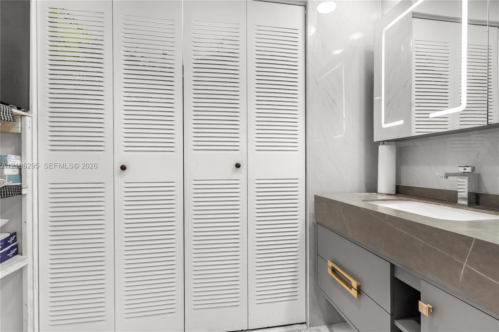 Floating vanity with a solid surface countertop, rectangular under-mount sink, matte chrome faucet, illuminated medicine cabinet, and white louvered-panel closet doors