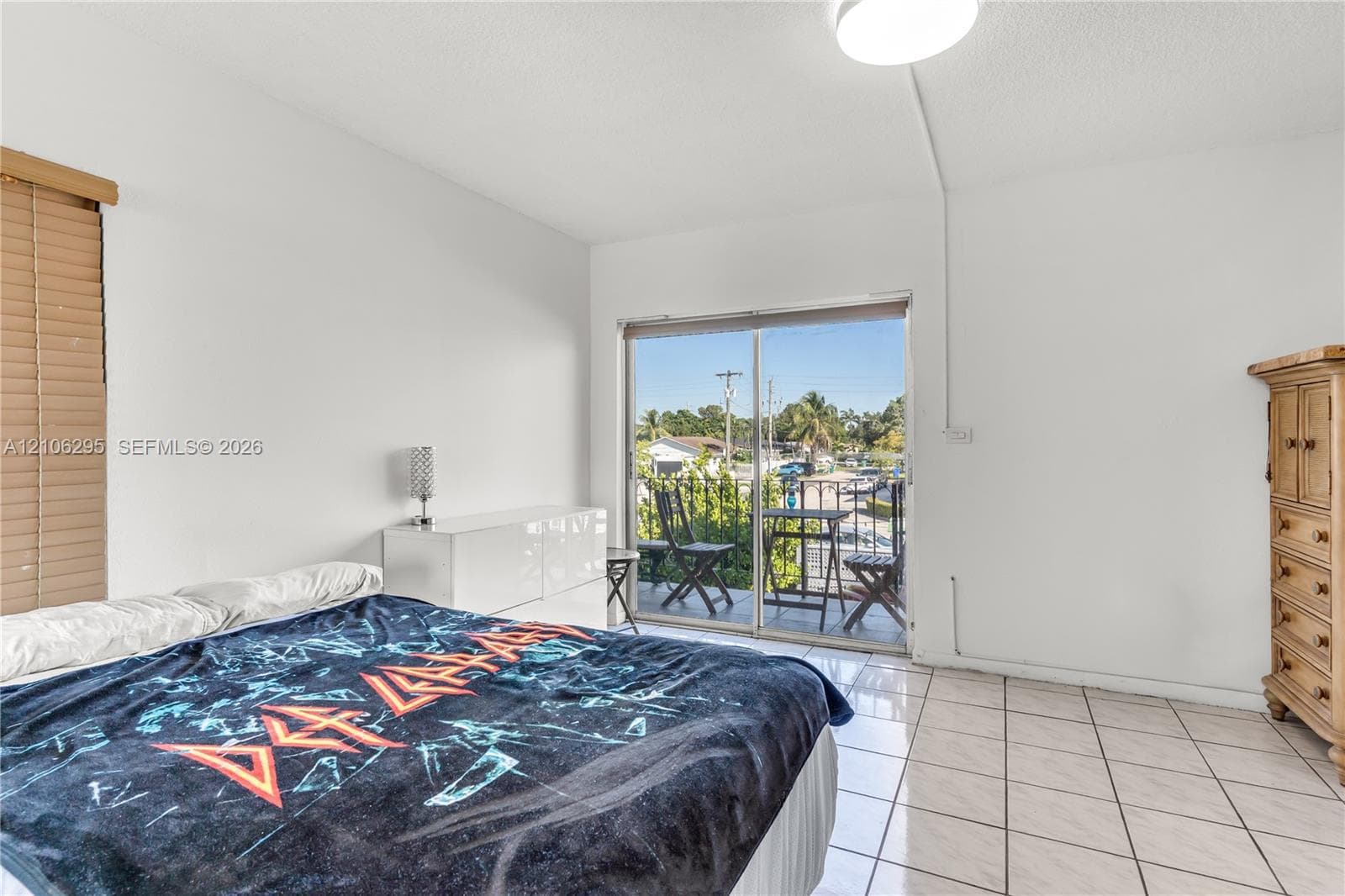 Interior space featuring tile flooring, sliding glass door access to a balcony, and a window with wood-finish blinds