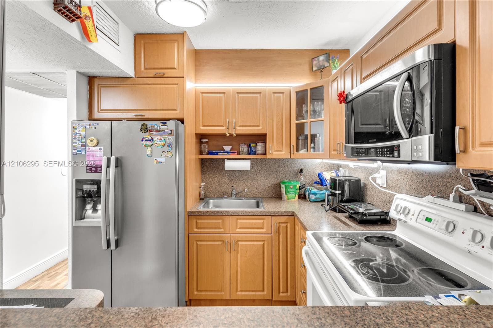 Kitchen featuring wood cabinetry, stainless steel side-by-side refrigerator, built-in microwave, integrated under-cabinet lighting, and stone-finish countertops