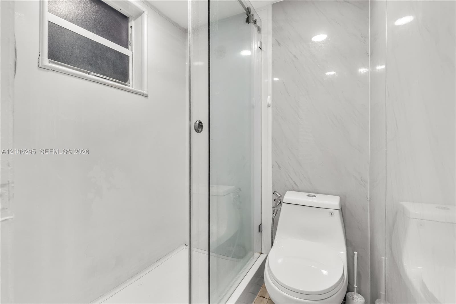 Full-height shower enclosure with a glass door, floor-to-ceiling veined tile surround, high-profile white toilet, and recessed lighting