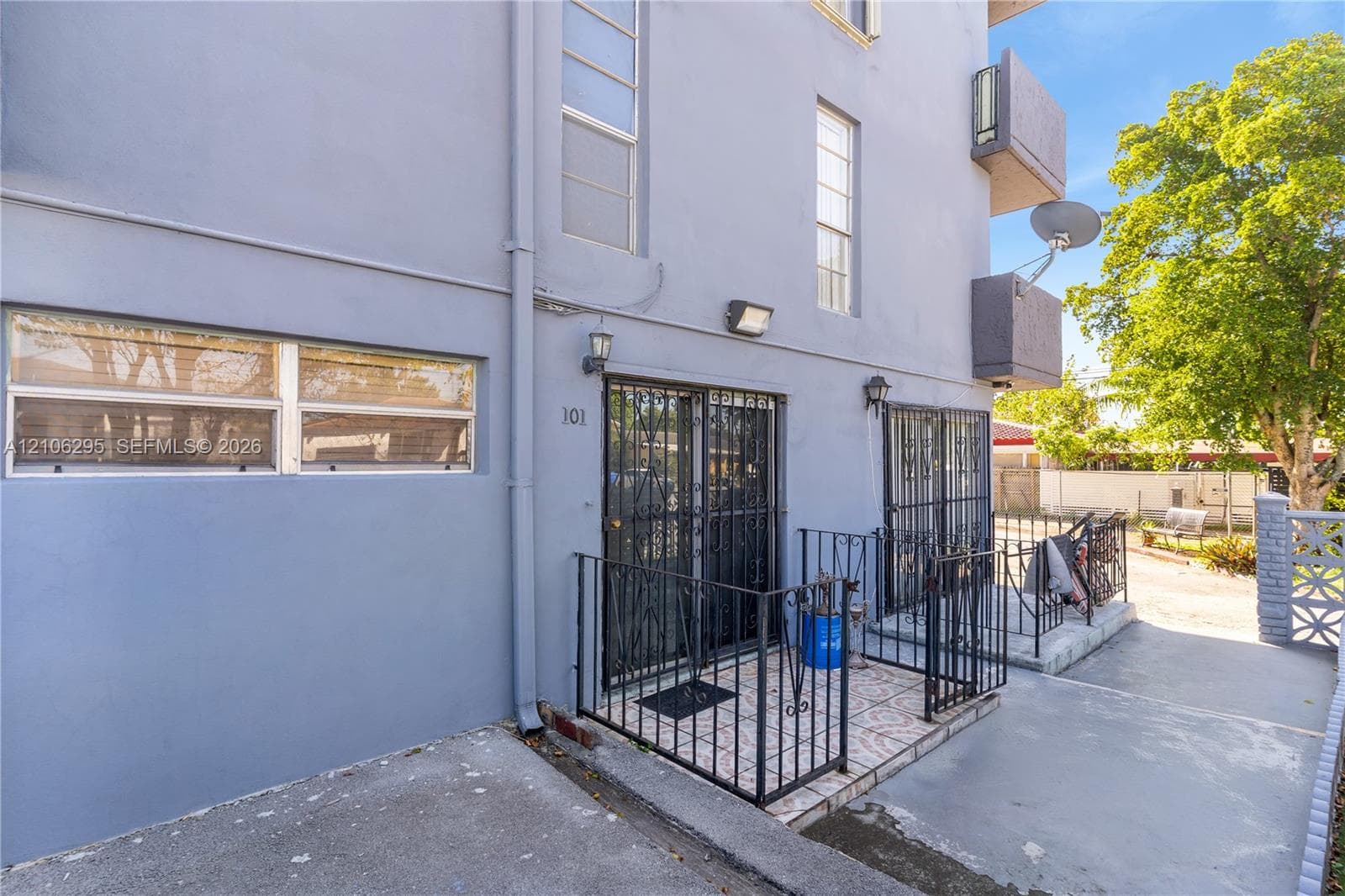 Exterior facade featuring smooth-finish stucco, metal security screen doors, railed entry patios with tile flooring, and wall-mounted exterior lighting fixtures