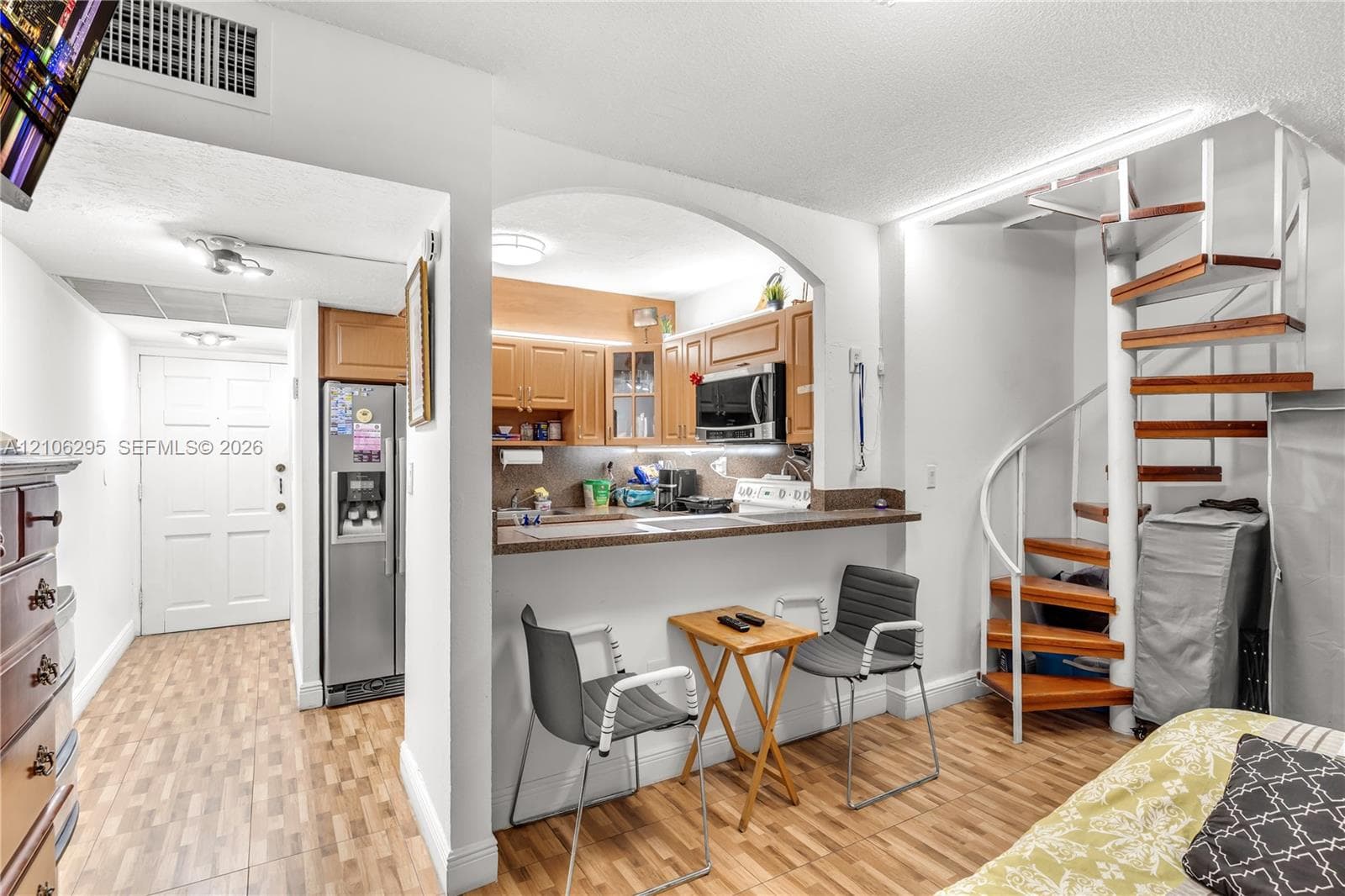 Kitchen featuring wood cabinetry, laminate countertops, and a pass-through breakfast bar, complemented by a spiral staircase with wood-finish treads and white metal railings, set over wood-finish flooring