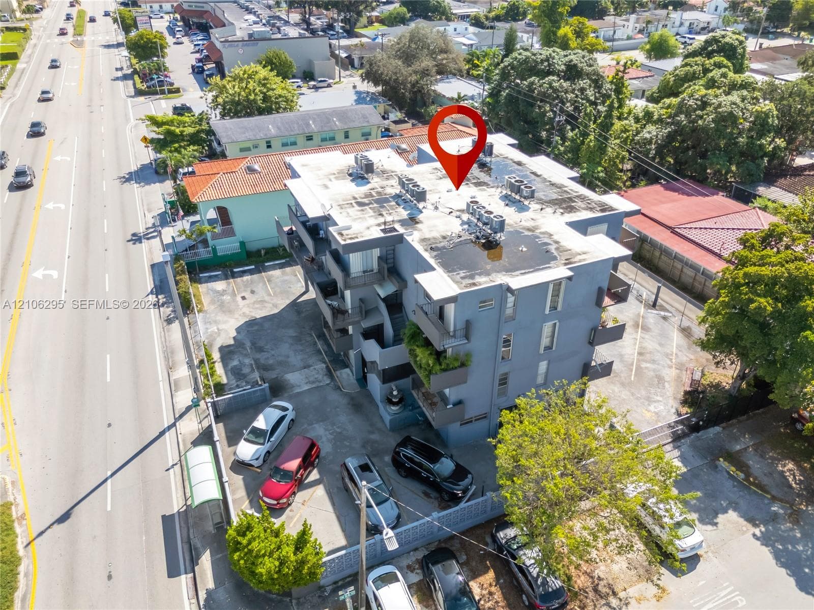 Multi-story structure featuring exterior balconies, a flat roof, and a paved surface-level parking area