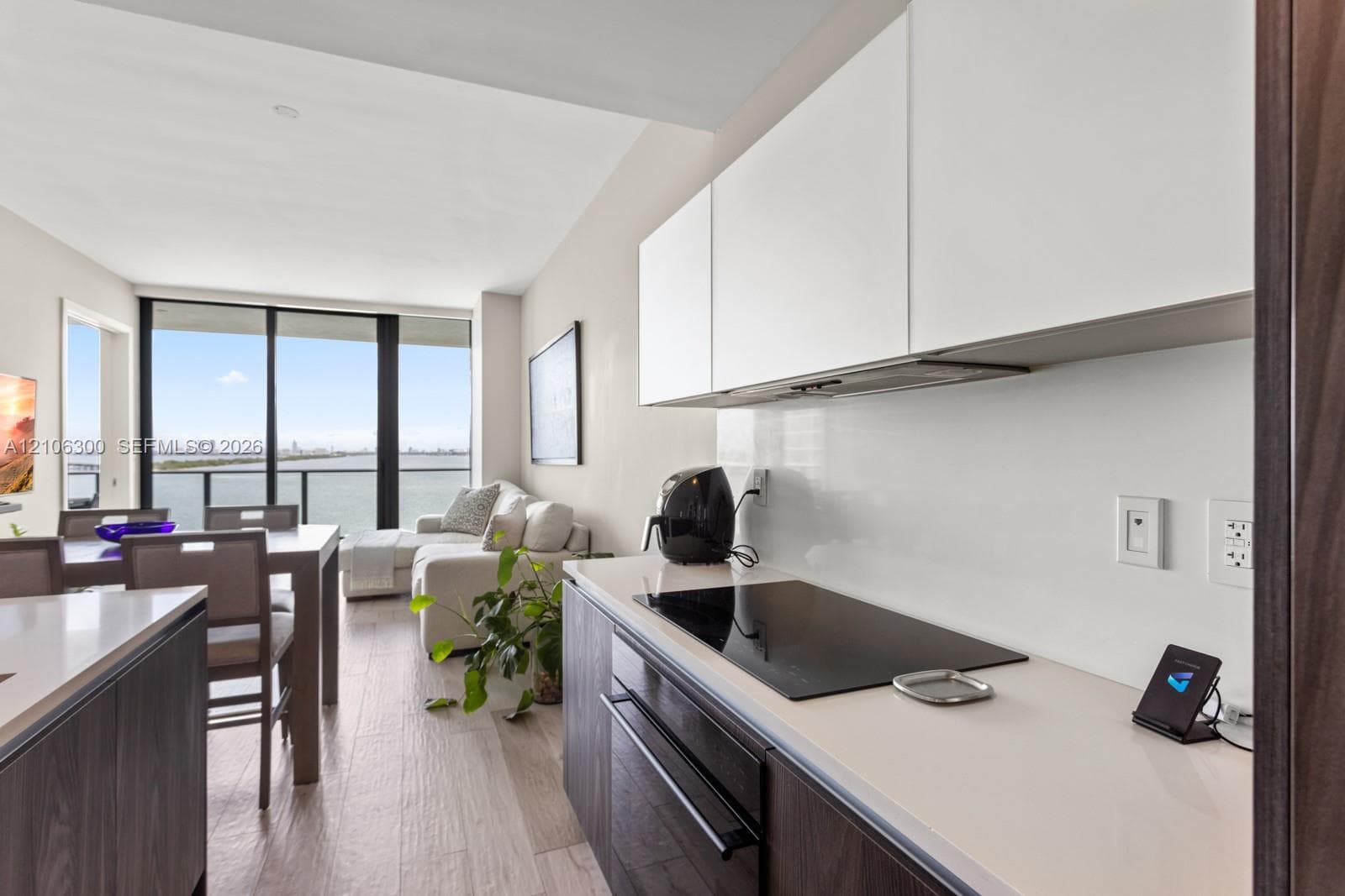 Modern kitchen featuring flat-panel cabinetry, light-toned countertops, a glass-ceramic cooktop, and wood-finish flooring with floor-to-ceiling windows
