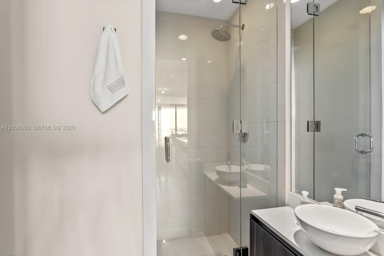 Walk-in shower with floor-to-ceiling tile, frameless glass enclosure, and a ceiling-mounted rainfall showerhead, accompanied by a floating vanity featuring dual vessel sinks and polished countertops