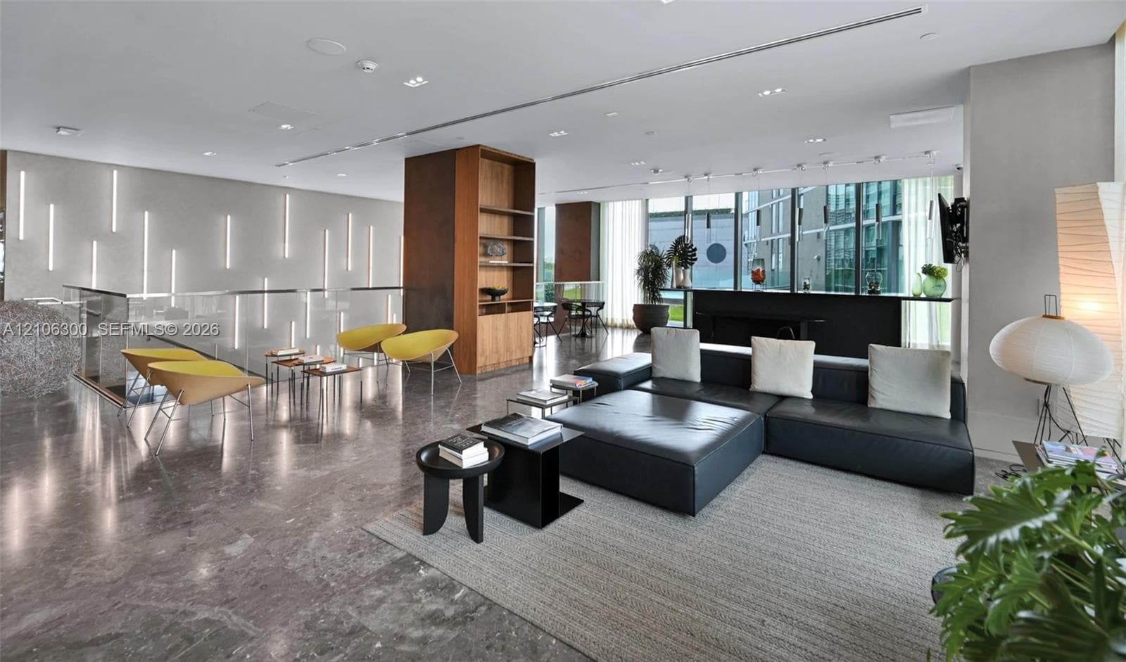 Open-concept interior featuring polished stone flooring, recessed ceiling lighting, floor-to-ceiling windows, built-in wooden shelving, and vertical wall-mounted accent lighting