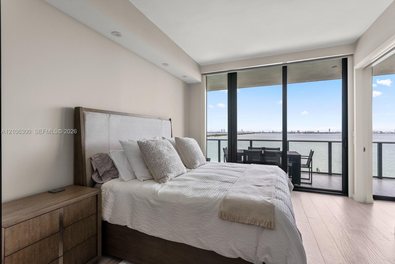 Floor-to-ceiling windows, wood-finish flooring, recessed lighting, and a private balcony with water backdrop